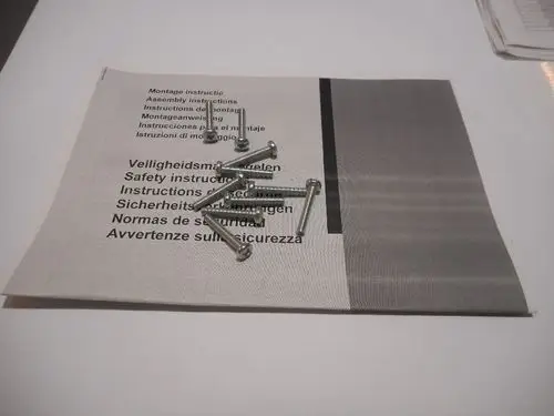 Schrauben von Remeha liegen auf einer Anleitung. Die Anleitung zeigt Montage- und Sicherheitsinformationen in mehreren Sprachen.